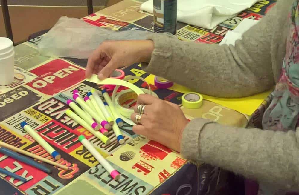 A person at a table working on a craft project with markers, tape, and paper.
