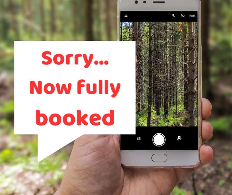 A hand holding a smartphone displaying a forest scene on its screen, overlaid with a white text box saying "sorry... now fully booked for free sessions.