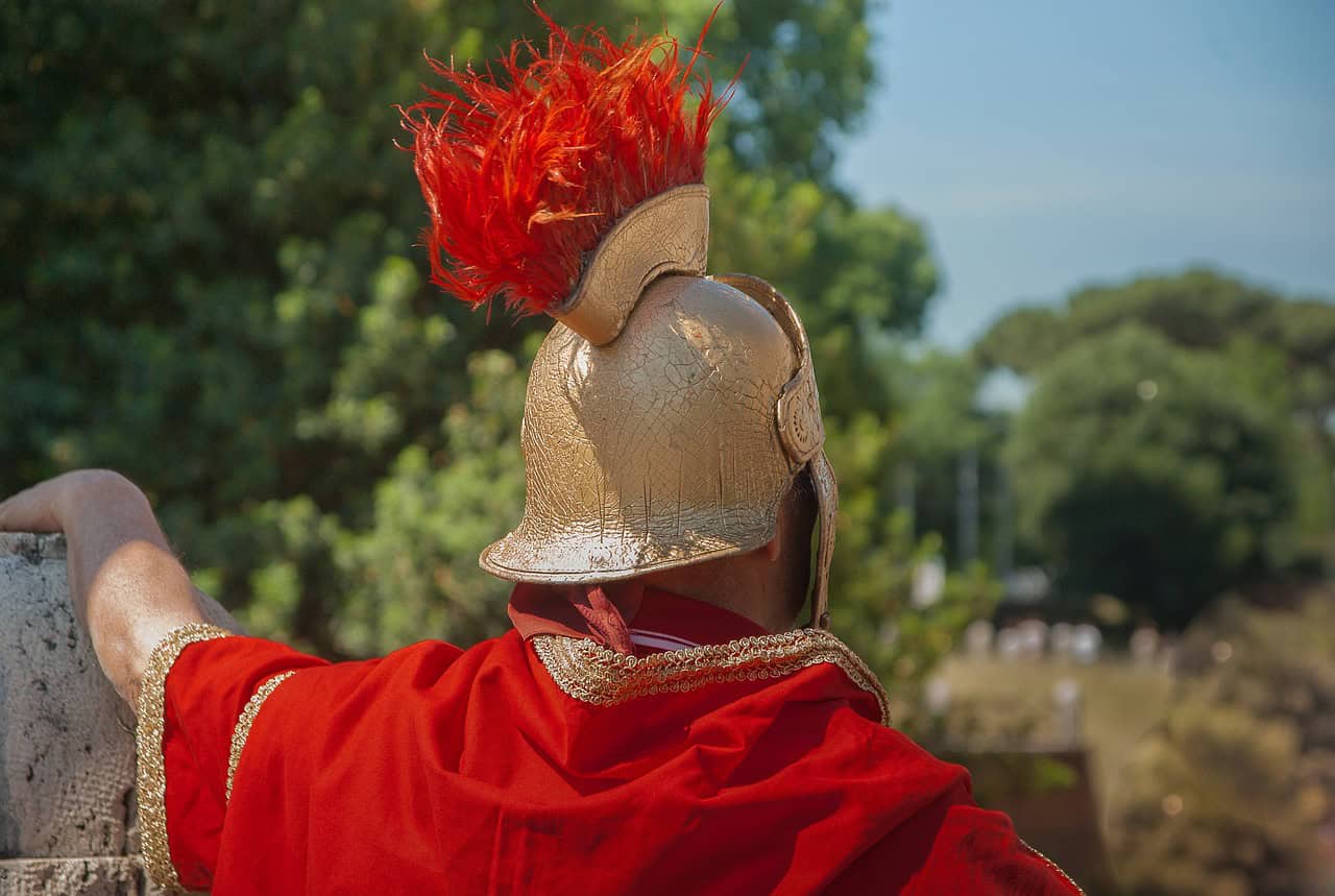 A person wearing a traditional Roman centurion helmet with a red feather plume and a red cloak views a landscape during a hidden history tour, symbolizing historical or cultural reenactment.
